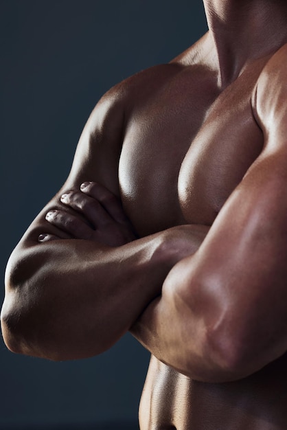 Muscles on muscles Closeup shot of an unrecognizable and athletic young mans chest while he poses arms folded in studio against a dark background