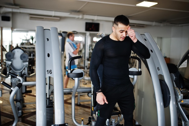 Muscular arab man training and doing workout on fitness machine in modern gym.