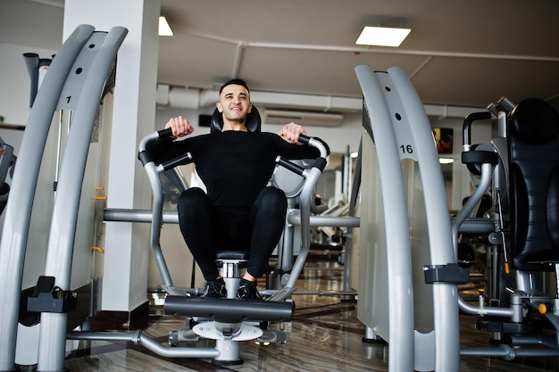 Muscular arab man training and doing workout on fitness machine in modern gym.