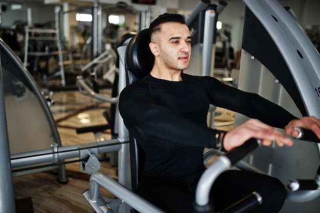 Muscular arab man training and doing workout on fitness machine in modern gym.