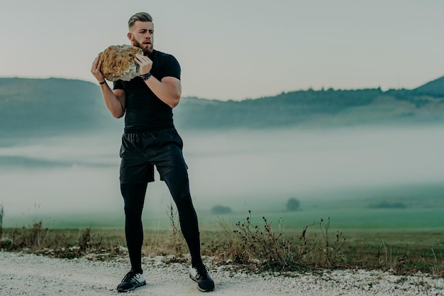 Muscular athlete man trains and exercises with big stone