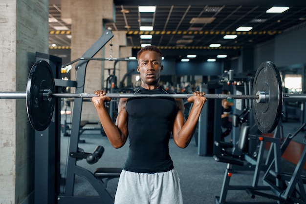 Muscular athlete in sportswear doing exercise with barbell on training in gym. Workout in sport club, healthy lifestyle