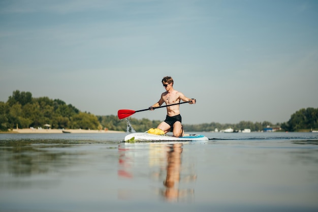 Muscular athlete trains in swimming on the river on a sup board actively rowing with a paddle with a serious face