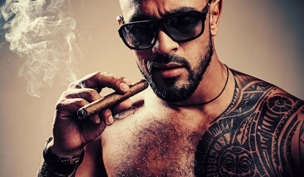 Muscular athletic sexy male with naked torso Brutal handsome man with tattooed body Stylish bearded man A beautiful and charming man with sunglasses Dark Sunglasses