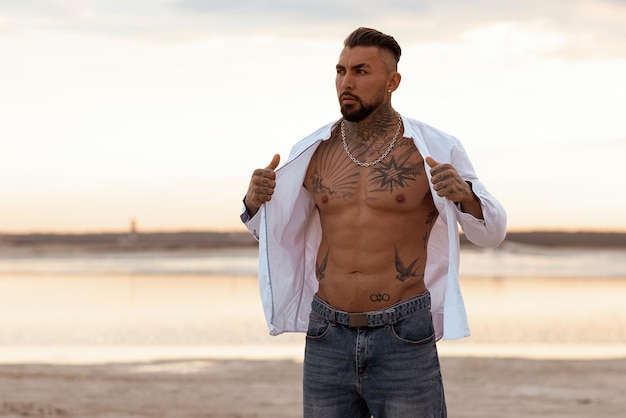 Muscular athletic sexy man in white shirt with bare chested rests on beach