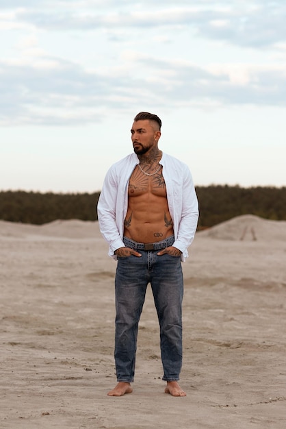 Muscular athletic sexy man in white shirt with bare chested rests on beach