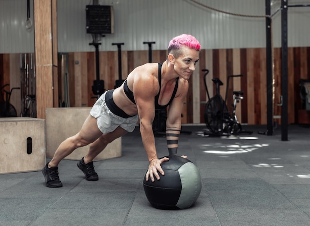 Muscular athletic woman push ups with medicine balls in a modern gym. Cross fit, functional training