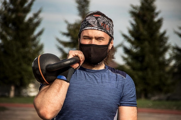 Muscular bearded male athlete workout outdoor with kettlebell we