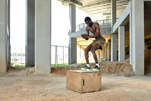 Muscular black athlete jumping on wooden box Urban background