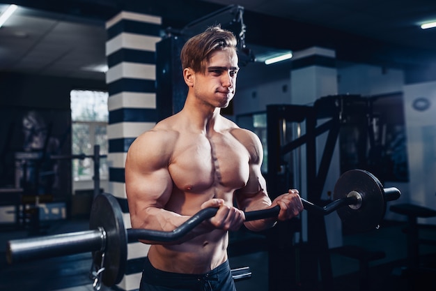 Muscular bodybuilder guy doing exercises on biceps with big dumbbell in gym