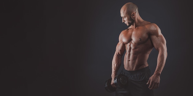 Muscular and fit young bodybuilder fitness male model posing over black background copy space