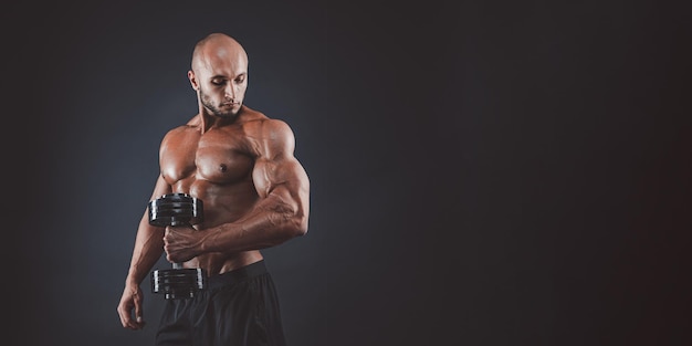 Muscular and fit young bodybuilder fitness male model posing over black background copy space