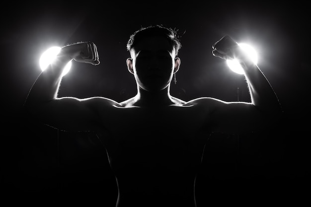 Muscular fitness man exercises healthy lifestyle in dark background silhouette back light