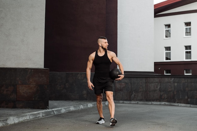 Muscular fitness trainer is walking with a heavy fitball outdoors