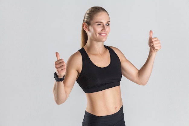 Muscular girl showing thumbs up at camera and wink