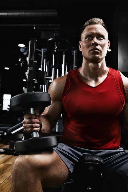 Muscular guy bodybuilder doing exercises with dumbbells close-up in the gym. Athletic body, healthy lifestyle, fitness motivation, positive body.