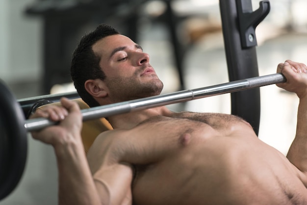 Muscular Hairy Man Doing Heavy Weight Exercise For Chest With Barbell In Gym