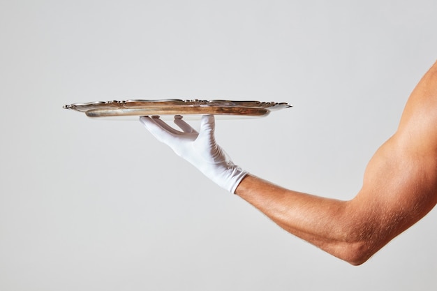 Muscular hand of waiter in a white glove holding a silver vintage empty tray