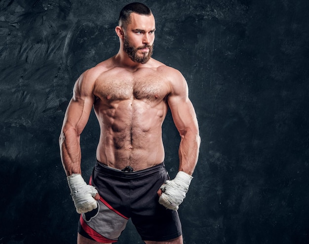 Muscular handsome fighter with naked torso is demonstraiting his power at dark photo studio.