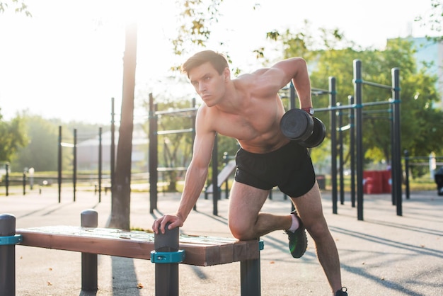 Muscular male athlete with arms raised doing lifting exercises dumbbells