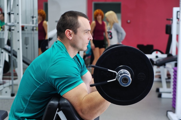 Muscular man doing exercises for biceps with barbell on Scott's bench