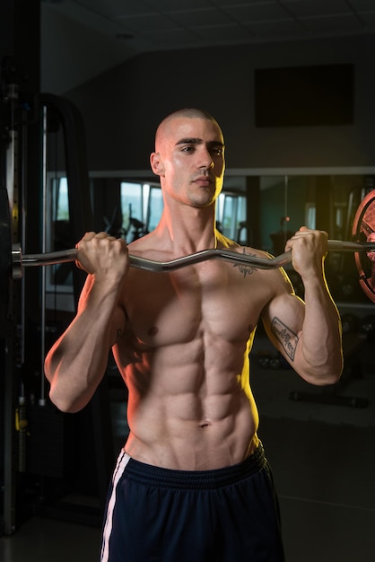 Muscular Man Doing Heavy Weight Exercise For Biceps With Barbell In Gym