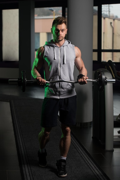 Muscular Man Doing Heavy Weight Exercise For Biceps With Barbell In Gym