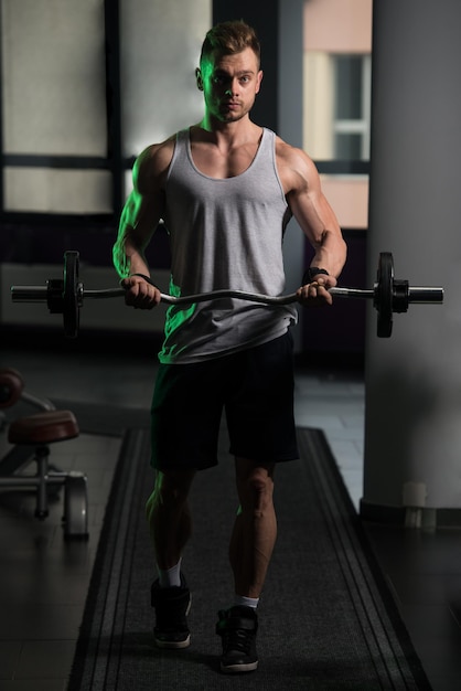 Muscular Man Doing Heavy Weight Exercise For Biceps With Barbell In Gym