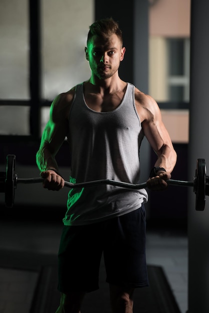 Muscular Man Doing Heavy Weight Exercise For Biceps With Barbell In Gym