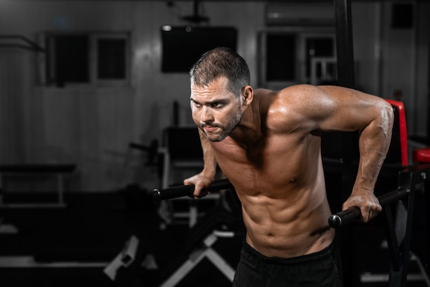 Muscular man doing push-ups on uneven bars in crossfit gym.