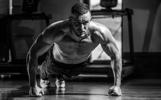 Muscular man doing pushups on one hand against gym background.