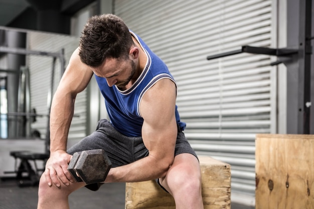 Muscular man lifting dumbbell on wooden block at the crossfit gym