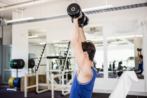 Muscular man lifting dumbbells on bench at the gym