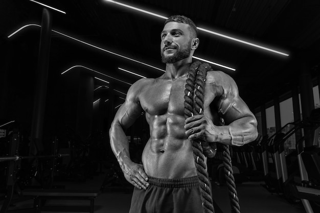 Muscular man posing in the gym with a rope. Fitness concept.