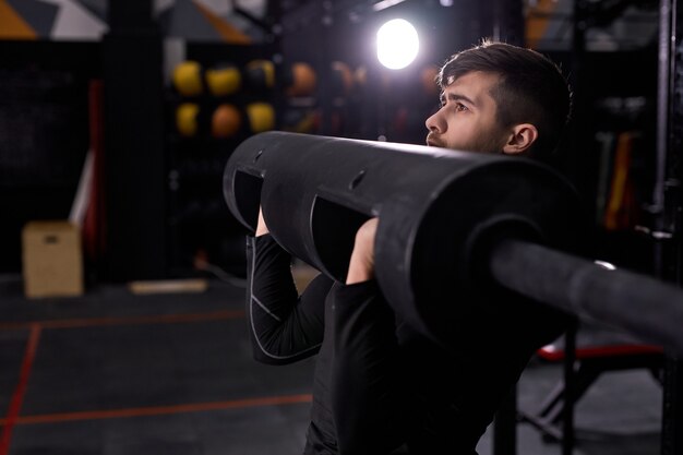 Muscular man raising heavy weights, training pumping arm muscles . strong man using sportive equipment in modern fitness center, gym. male wearing sportive outfit, concentrated on workout