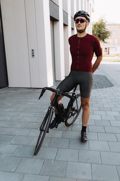 Muscular man in sport clothes safety helmet and mirrored glasses posing with his sport bike near modern building Concept of people workout and recreation