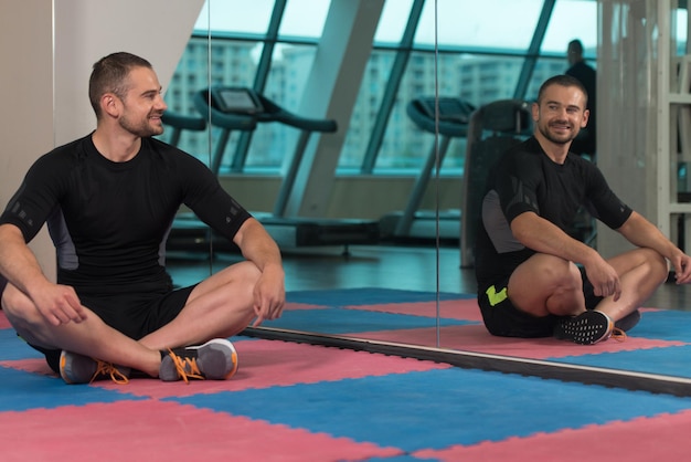 Muscular Man Stretches At The Floor In A Gym And Flexing Muscles  Muscular Athletic Bodybuilder Fitness Model