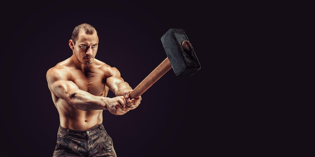 Muscular man with great anatomy posing on a black background with a big hummer in his hands