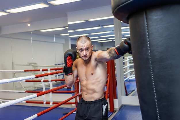 Muscular man with a naked torso in boxing gloves boxing a punching bag