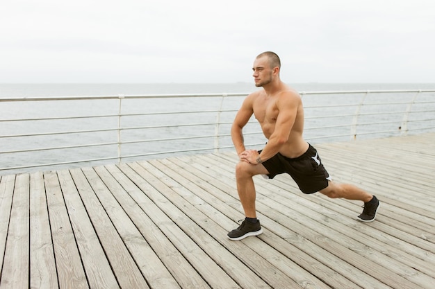 Muscular man with a naked torso doing leg stretch before training on the beach