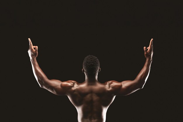 Photo a muscular man with raised arms back view in a celebratory pose against a black background