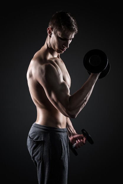 Muscular man working out doing exercises with dumbbells at biceps