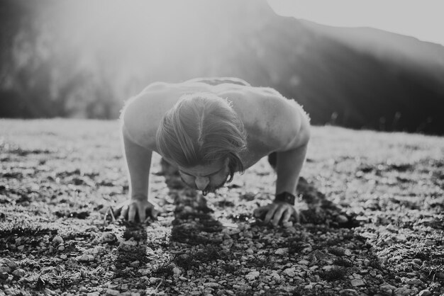 Muscular modern guy doing push-ups on top of mountain in nature.