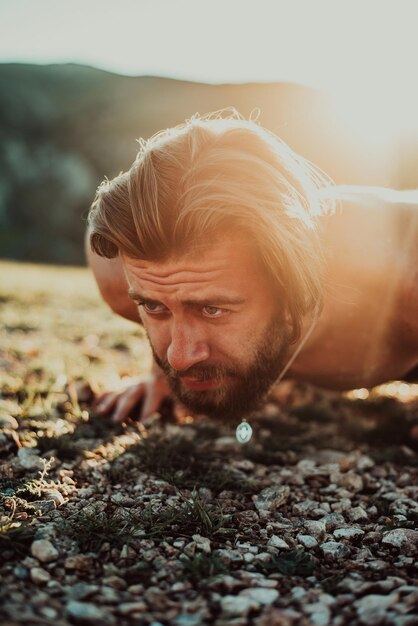 Muscular modern guy doing push-ups on top of mountain in nature.