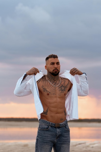 Muscular sexy young man taking off t shirt on empty white sand beach and turquoise ocean