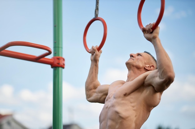 Muscular shirtless man doing pull ups on gymnastic rings