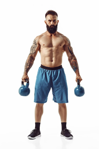 Muscular shirtless tattooed bearded male athlete bodybuilder workout with kettlebell on a white back