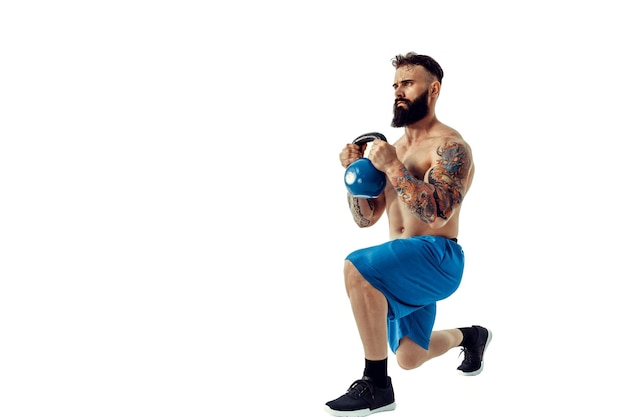 Muscular shirtless tattooed bearded male athlete bodybuilder workout with kettlebell on a white back