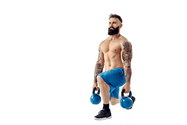 Muscular shirtless tattooed bearded male athlete bodybuilder workout with kettlebell on a white background Isolate