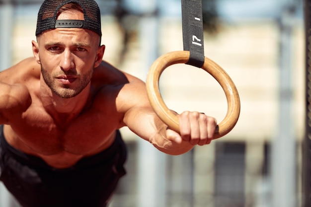 Muscular sportsman exercising on outdoor gymnastic rings in outdoor gym Hands at rings dipping man doing exercise using rings